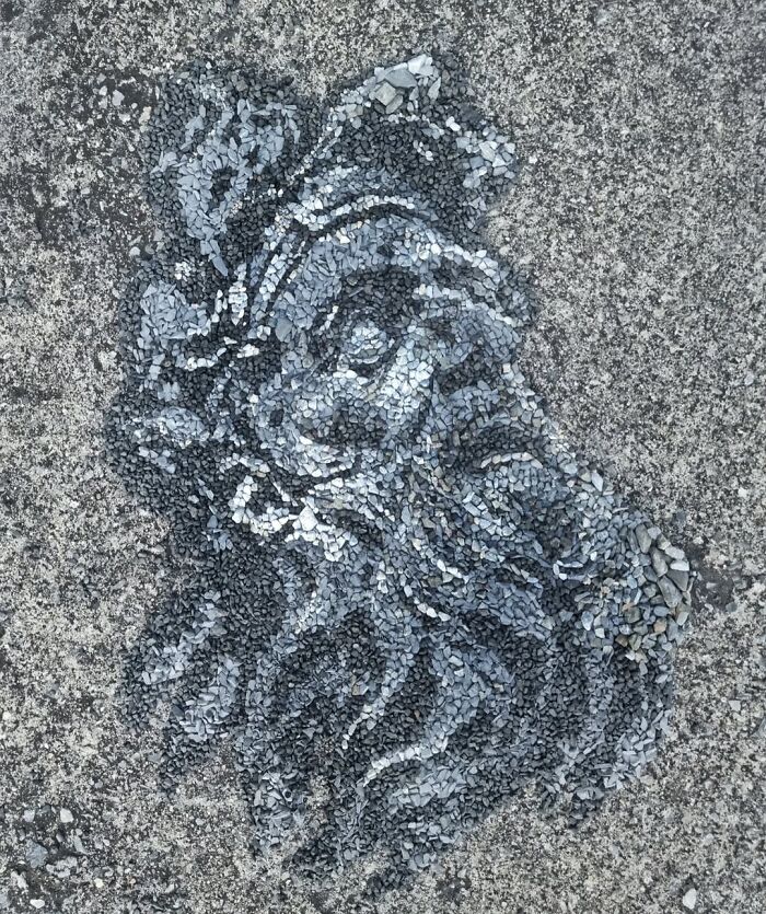 Intricate temporary mosaic of a face created with stones and pebbles by British artist.