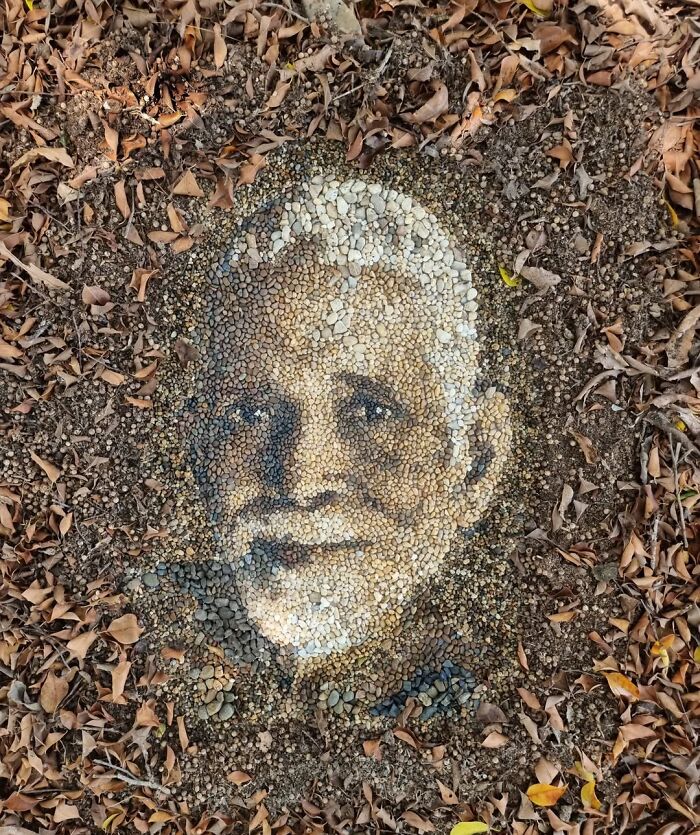 Pebble mosaic portrait on forest floor, crafted by British artist using stones and leaves for intricate detail.