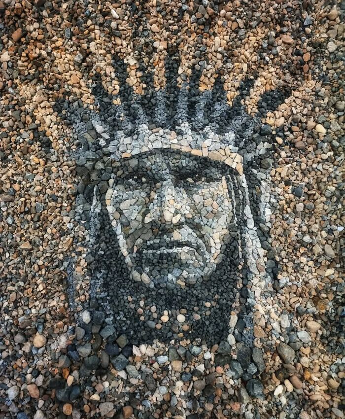 Intricate stone and pebble mosaic of a human face, showcasing British artist's temporary art style.