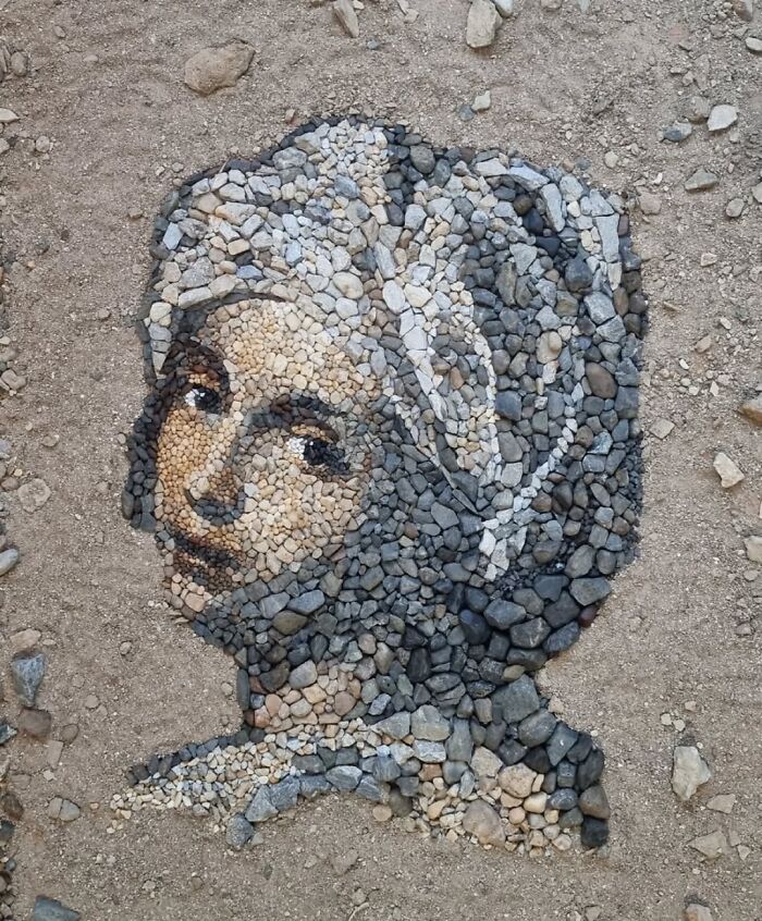 Intricate temporary mosaic portrait created using stones and pebbles by a British artist on sandy ground.