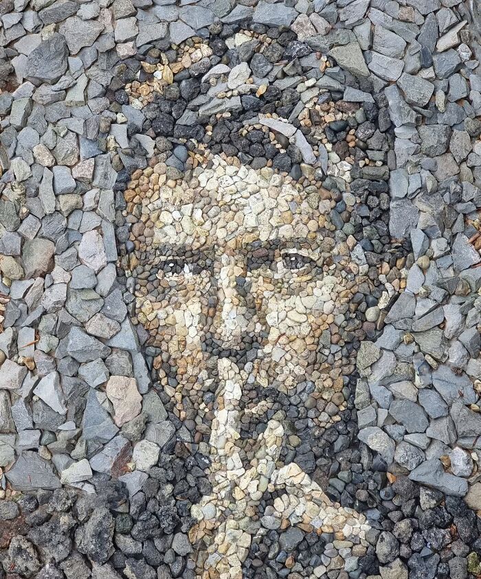 Intricate temporary mosaic created from stones and pebbles by a British artist, depicting a face in shades of grey and brown.