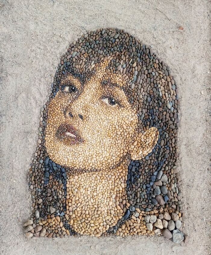 Intricate mosaic portrait of a woman made from stones and pebbles by British artist on sand background.