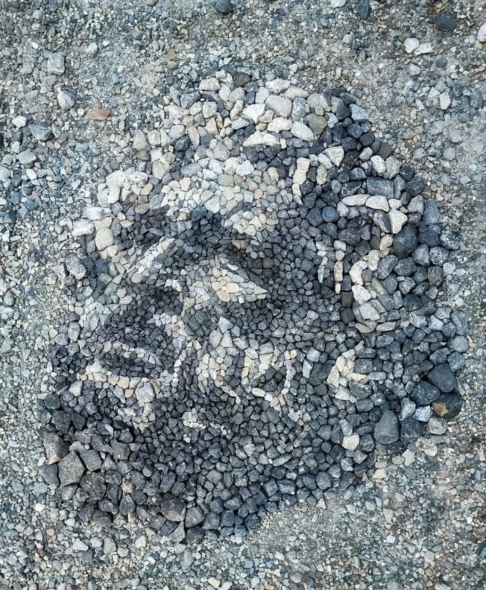 Intricate temporary pebble mosaic by British artist on gravel surface.