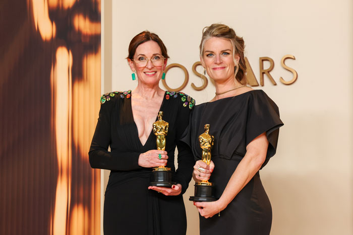 Two women holding Oscar trophies at the 2025 Oscars ceremony, standing in front of a backdrop with the word "Oscars.
