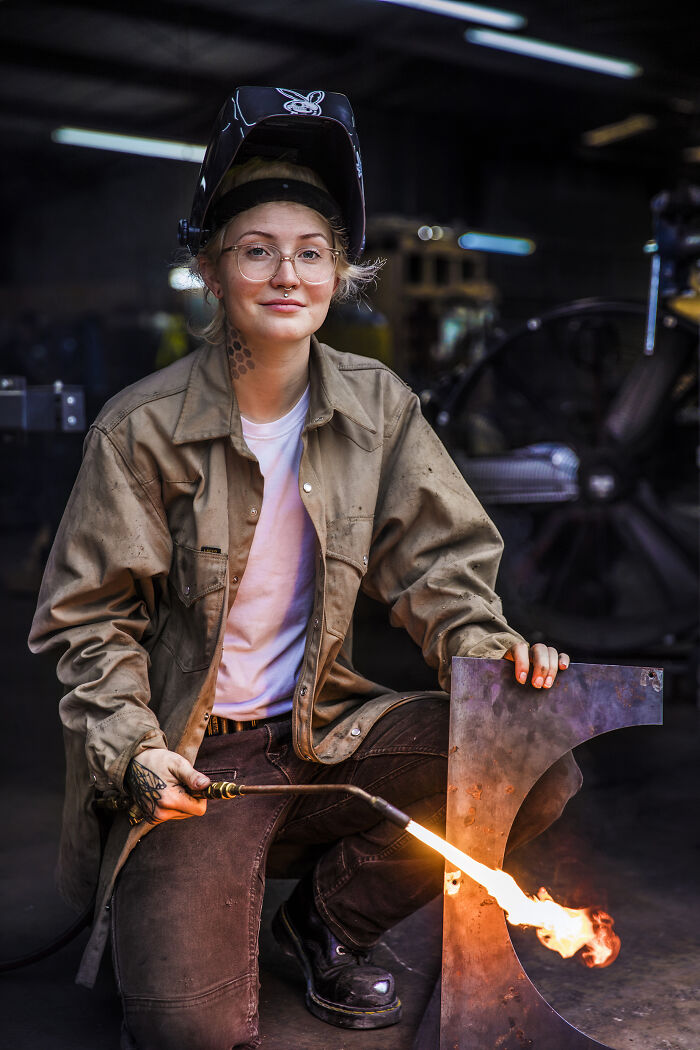 Female welder with torch and helmet, challenging societal norms in workshop setting.