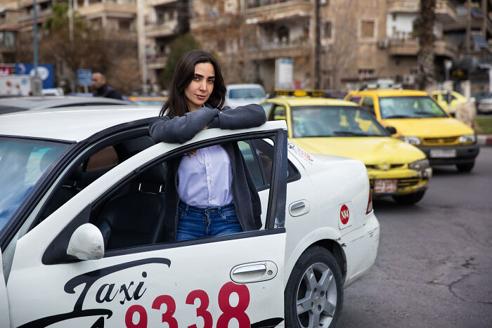 A woman standing confidently beside a taxi, surrounded by city traffic, challenging societal norms.