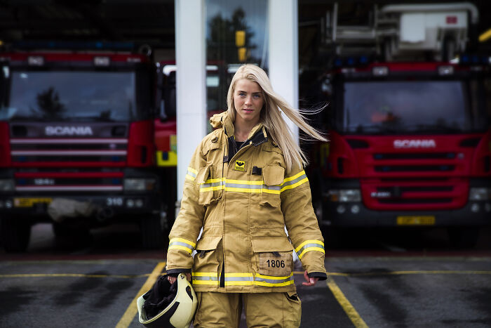 Woman firefighter in gear stands confidently outside a fire station, representing women defying societal norms.