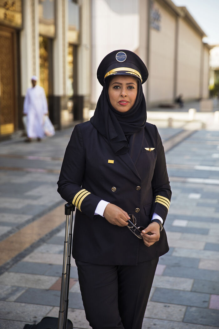 Female pilot in uniform standing confidently with a suitcase, exemplifying women defying societal norms.