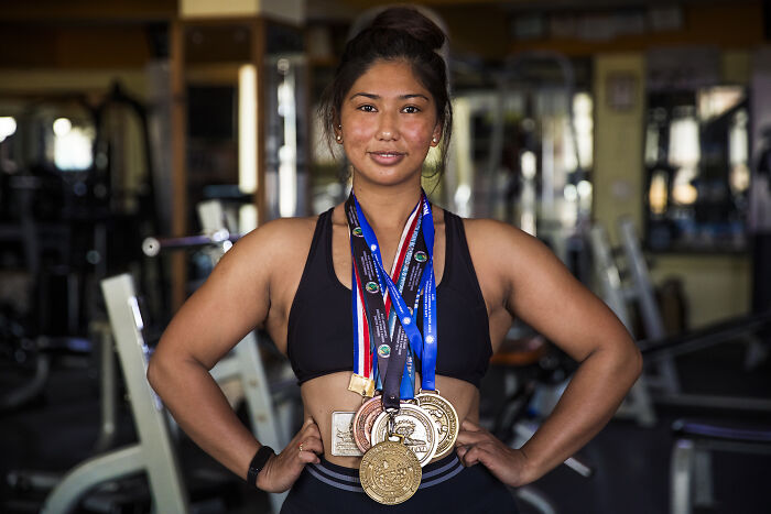 Woman in gym wearing multiple medals, showcasing women defying societal norms.