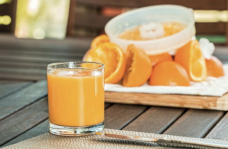 Glass of fresh orange juice on wooden table with sliced oranges in the background, illustrating morning freshness.