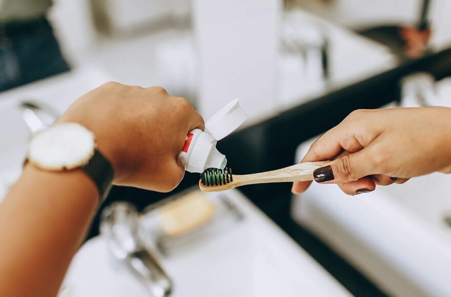 Applying toothpaste on a toothbrush in a bathroom, highlighting a nighttime routine debate.