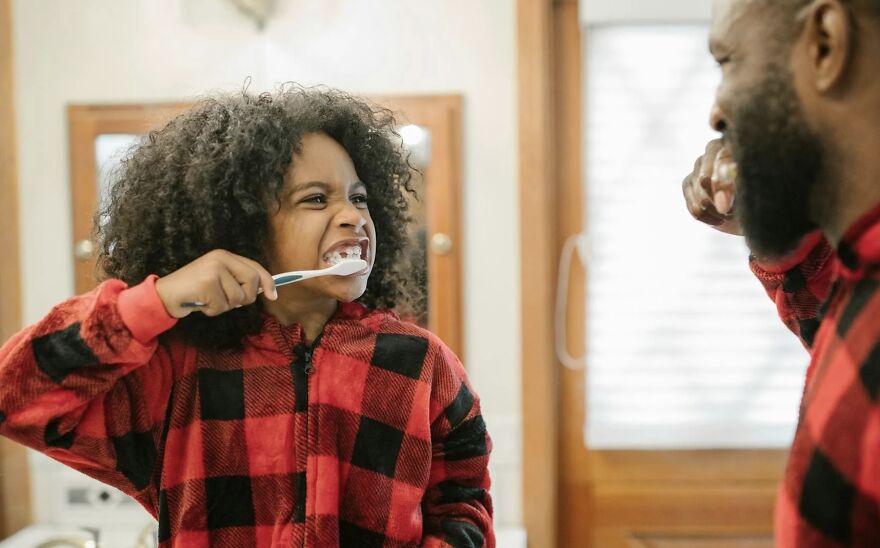 Child in pajamas brushing teeth with parent, highlighting morning routine debate.