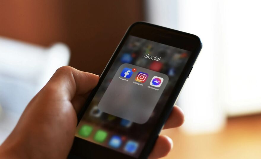 Person holding a smartphone with social media app icons displayed on screen.