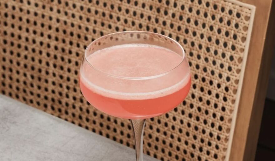A pink cocktail on a table with a woven chair backdrop, highlighting evening relaxation benefits.