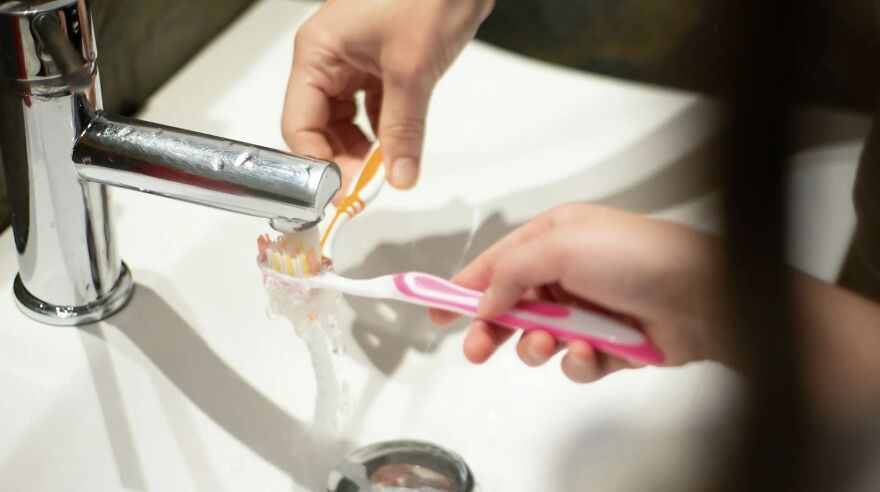 Person brushing teeth at sink, debating showering at night, water flowing from faucet.