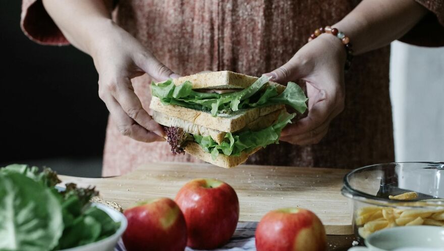 Person preparing a lettuce sandwich with apples nearby on a wooden board.