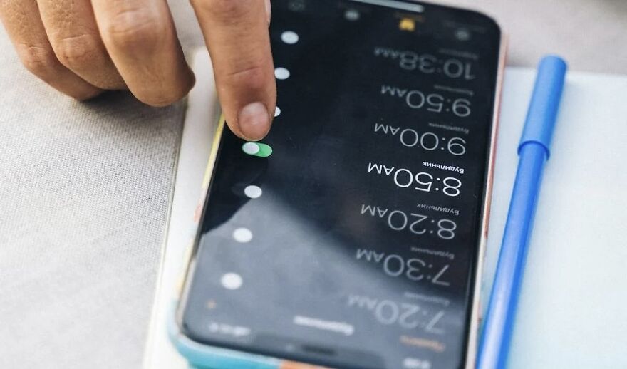 Finger adjusting morning alarms on a smartphone, highlighting the night shower vs. morning debate.