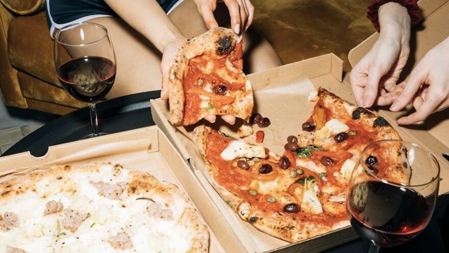 People enjoying pizza and red wine at night, with pizza boxes on a table.