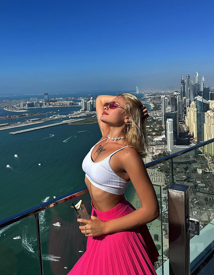 Model posing on a balcony overlooking the ocean and cityscape, linked to trafficking investigation at "Porta Potty" parties.