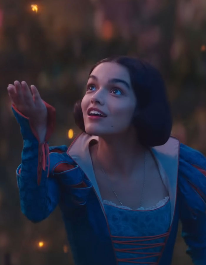 Young woman in a blue costume reaching out with an expression of wonder.