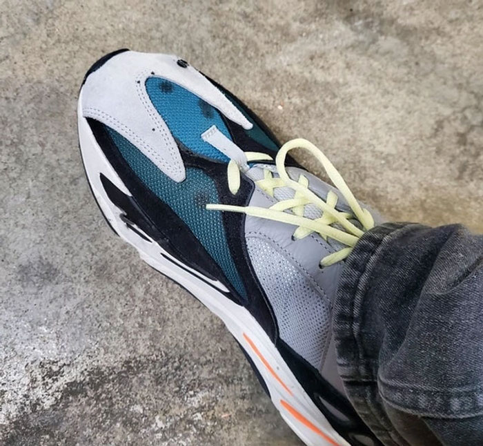 Sneaker with a folded sole and mismatched laces worn by a person on a concrete floor, highlighting worst colleagues humor.