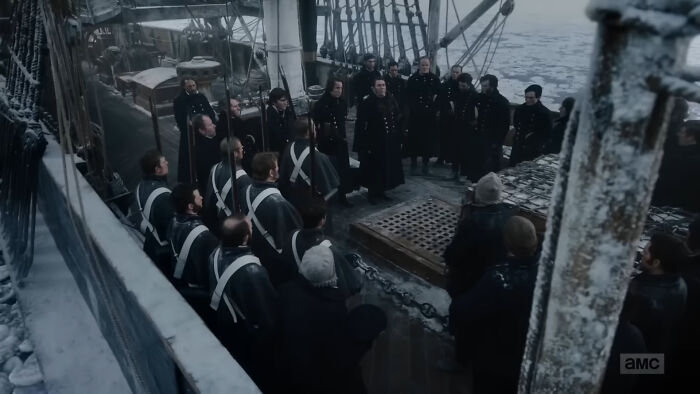 Crew on a historic ship's deck gathered in a snowy, cold environment, depicting a scene from the dark side of history.