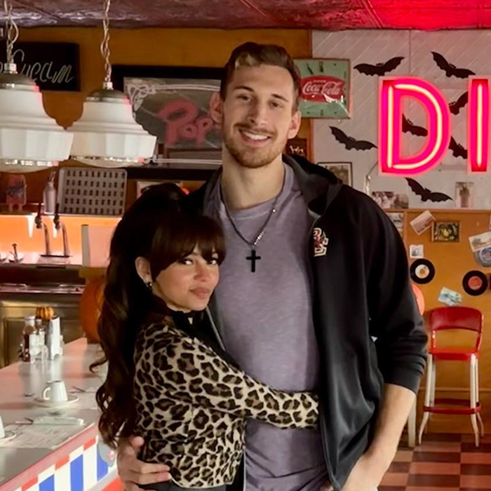 A Vanessa Morgan and James Karnik embracing in a retro diner setting with neon lights and vintage decor.