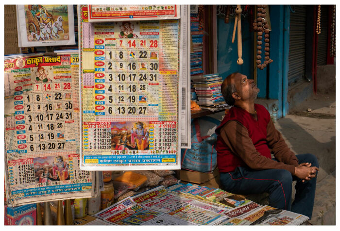 Man sitting by a street calendar stall, capturing raw, unfiltered moments in vibrant city life.