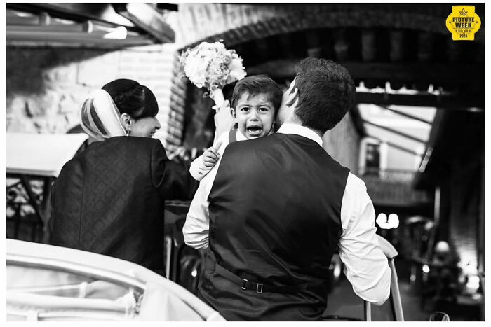A groom carries a crying child at a wedding, capturing a precious moment of love in this outstanding wedding photograph.