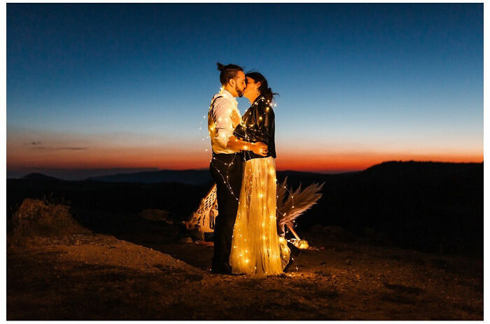 Couple embracing at sunset wrapped in fairy lights, capturing a precious wedding moment of love.