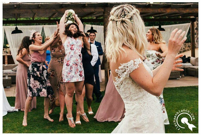 Guests in colorful dresses at a wedding joyfully catching a bouquet, captured by Jordi Tudela.