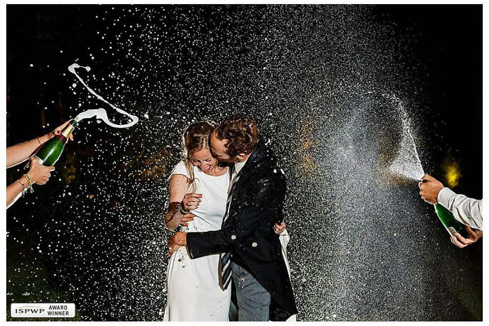 Bride and groom embrace under champagne spray celebrating love, captured in an outstanding wedding photograph by Jordi Tudela.