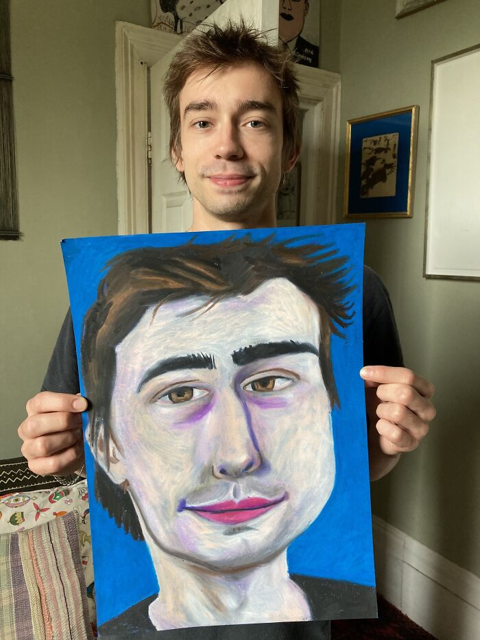 A British artist holds an expressive portrait with bold colors in a cozy room.