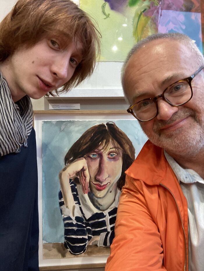 Two men posing with an expressive portrait painting at an art exhibit.