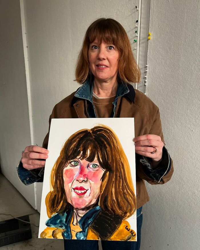 A British artist showcasing an expressive painted portrait, holding it proudly while standing in a studio.