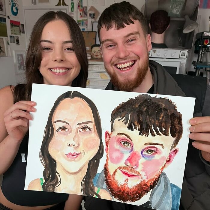 Smiling couple holds an expressive portrait by a British artist in a studio setting.