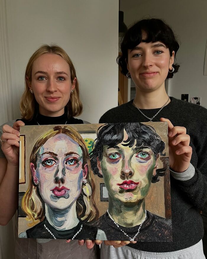 Two women holding expressive portraits painted by a British artist.