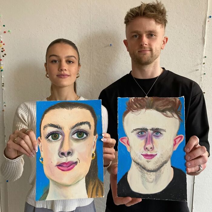 Two people holding expressive portraits by a British artist, showcasing vibrant and exaggerated features on a blue background.