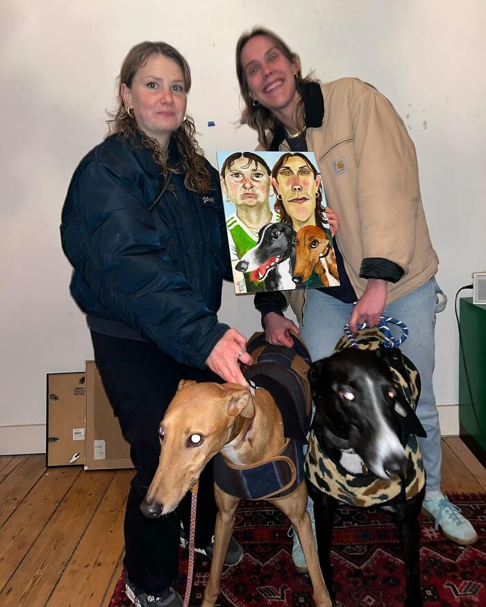 Two people holding a portrait of expressive art with two dogs in a room.