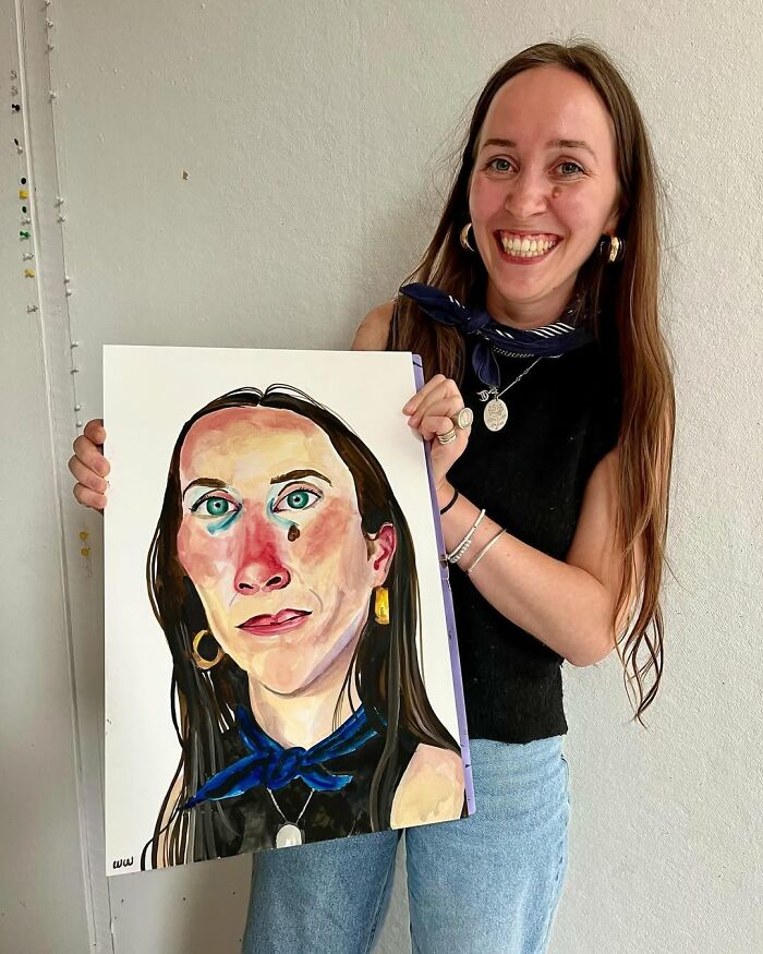 British artist showing her expressive portrait artwork, smiling beside the colorful painting she's holding.