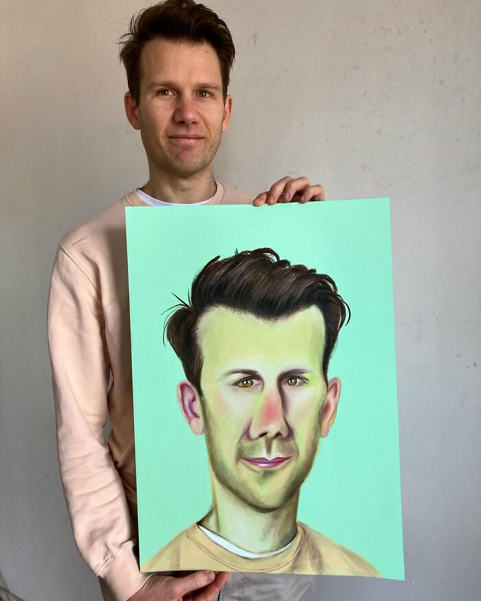British artist holding a colorful, expressive portrait against a neutral background.