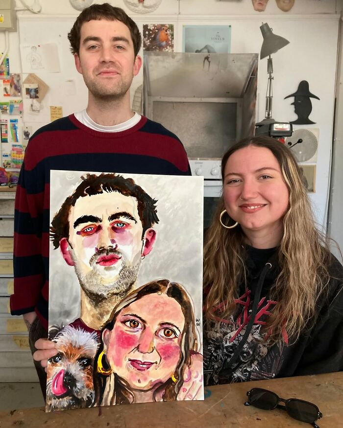 British artist displaying an expressive portrait painting while smiling in a workshop setting.