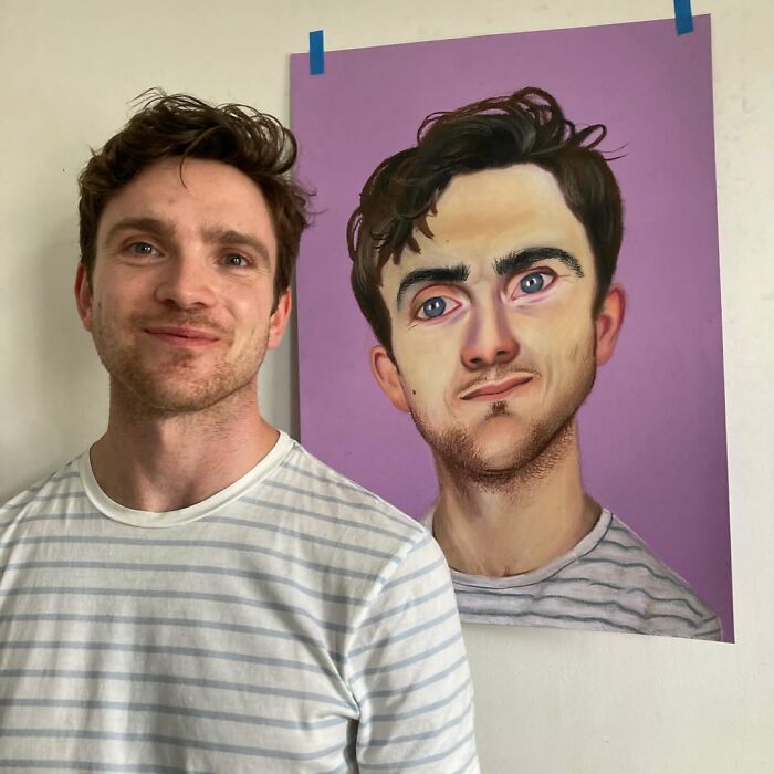 A British artist poses beside an expressive portrait he painted, with both subjects wearing striped shirts.