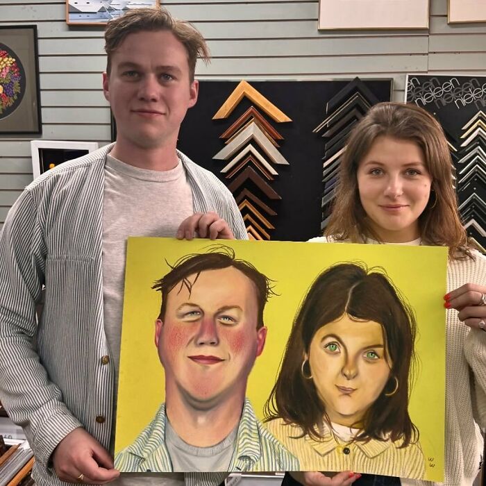 Two people hold an expressive portrait by a British artist, featuring their exaggerated facial features on a yellow background.