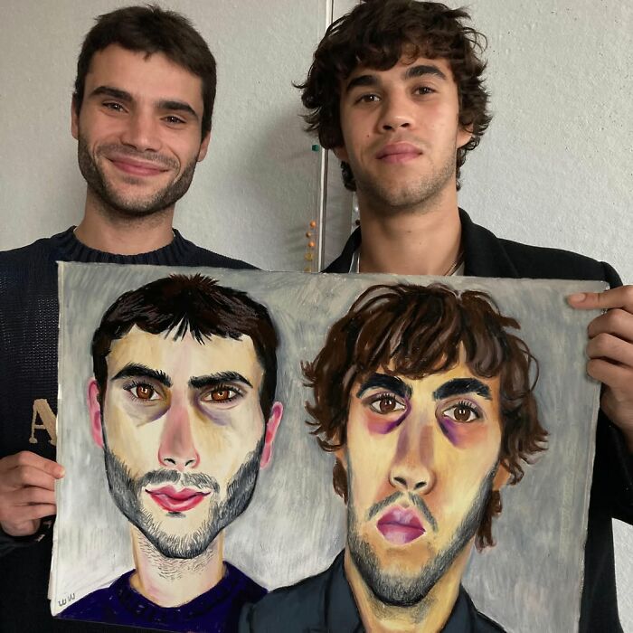 Two men holding an expressive portrait drawing that resembles them, highlighting the British artist's style.