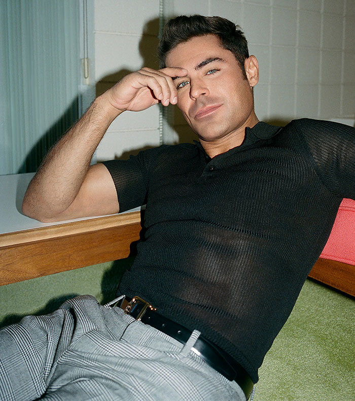 Man in a black shirt reclining, showcasing transformation with Zac Efron's aesthetic.