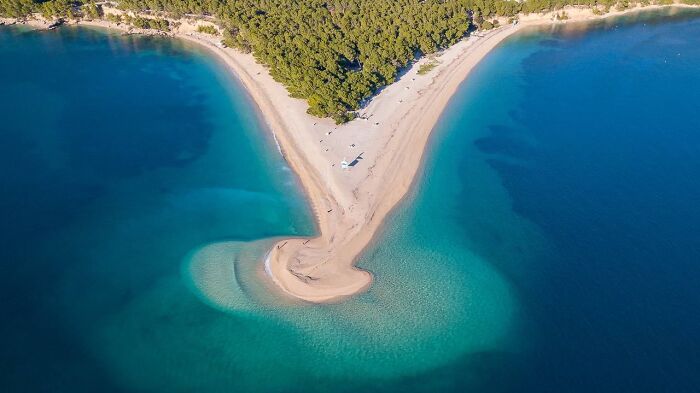 Aerial view of a stunning beach with turquoise waters and a forested backdrop.