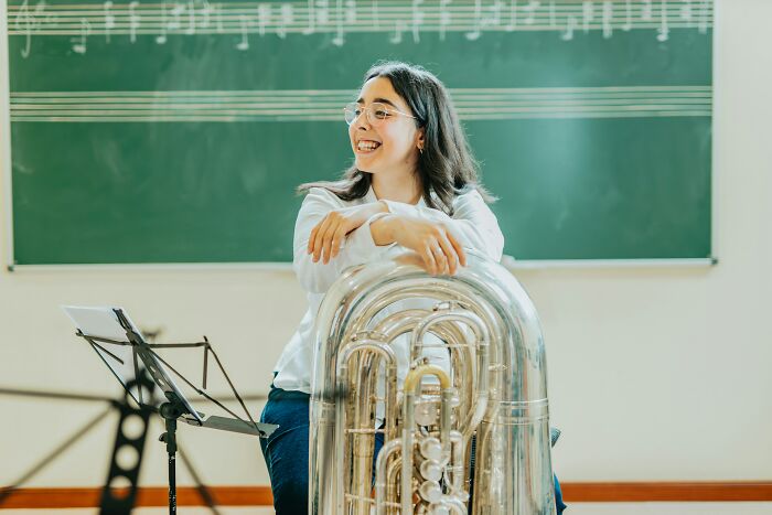 Musician smiling with a tuba in a music classroom, addressing job misconceptions.