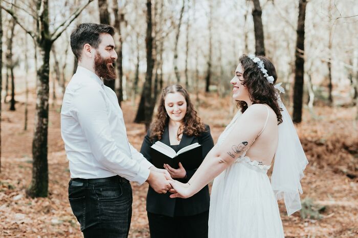 Bride and groom smiling in a woodland ceremony, holding hands without guest objections.