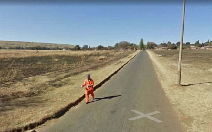 Person in orange suit walking down empty rural road found on Google Earth.